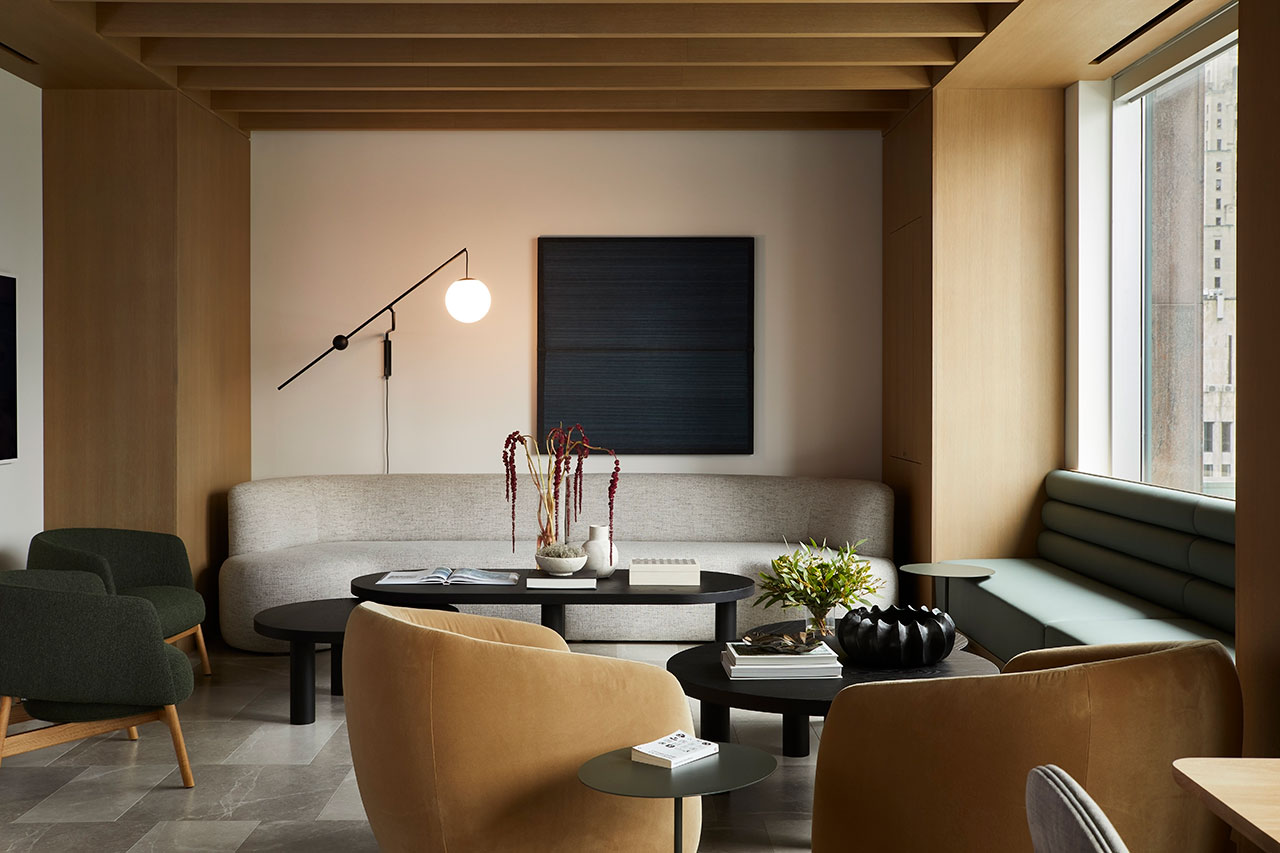 Modern office lounge with neutral tones, wood beams, and layered seating designed for informal gathering