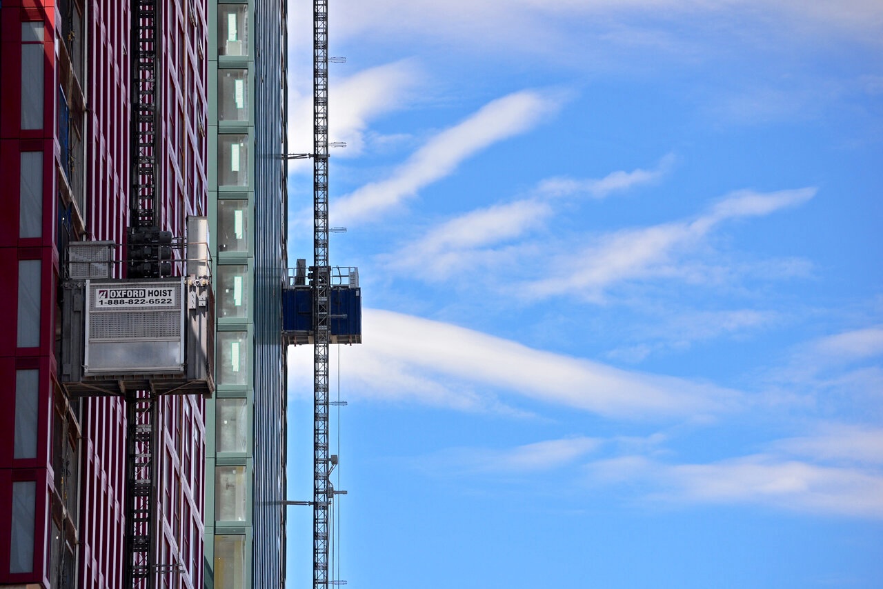 Two construction hoists project from the side of towers at the Rushden Station construction site in Toronto
