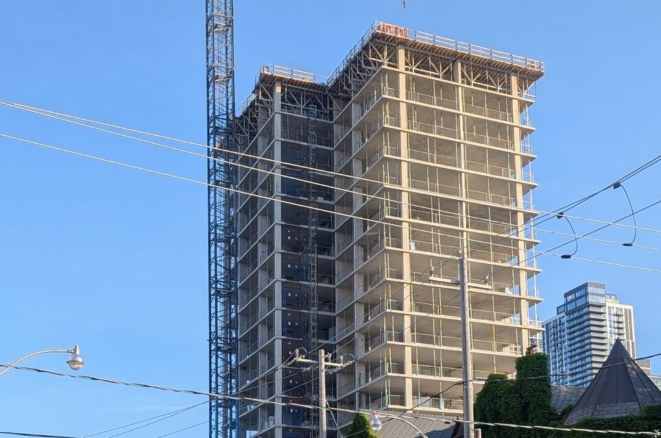 Hoem Garden District under construction in Toronto, showing tower crane, podium cladding progress, and the retained heritage house