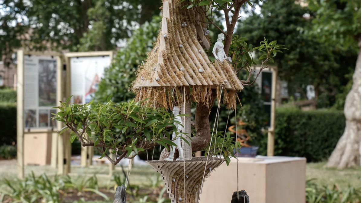 Miniature treehouse structures displayed among bonsai trees in a London park exhibition