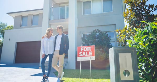 Couple standing in front of their home with a for sale sign
