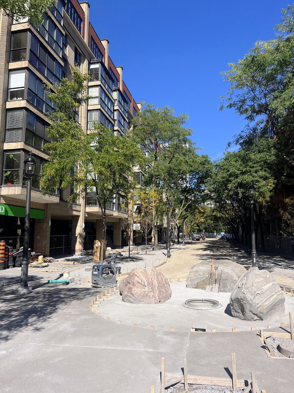 Boulders arranged around a circular concrete base forming a fountain at Market Lane Park, with timber edge forms and new sidewalk pours